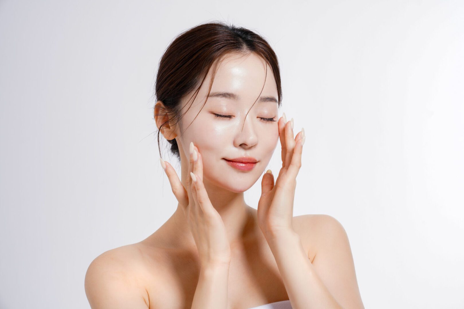 Woman applying skincare cream, eyes closed.