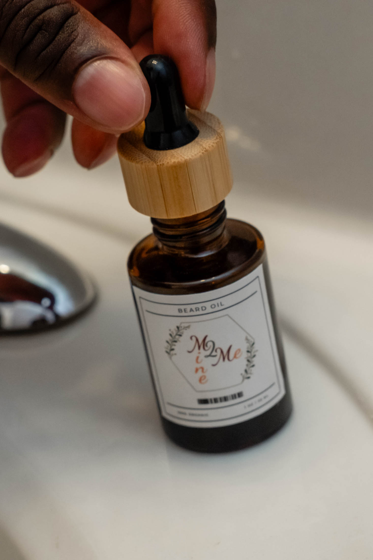 Hand holding dropper over beard oil bottle.