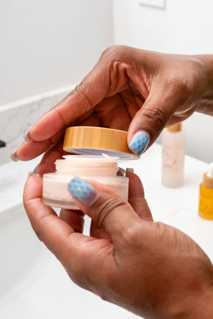 Hands opening a skincare cream jar.