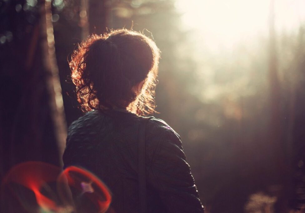Person standing in sunlit forest clearing.